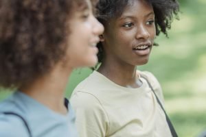 Two teenagers with curly hair chatting while walking outdoors in a park setting.