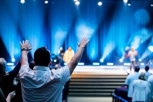 Group of people attending a lively worship service in a modern auditorium setting.