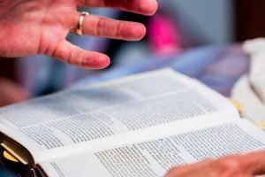 Close-up of hands engaged in Bible study at an indoor setting, promoting spiritual discussion.